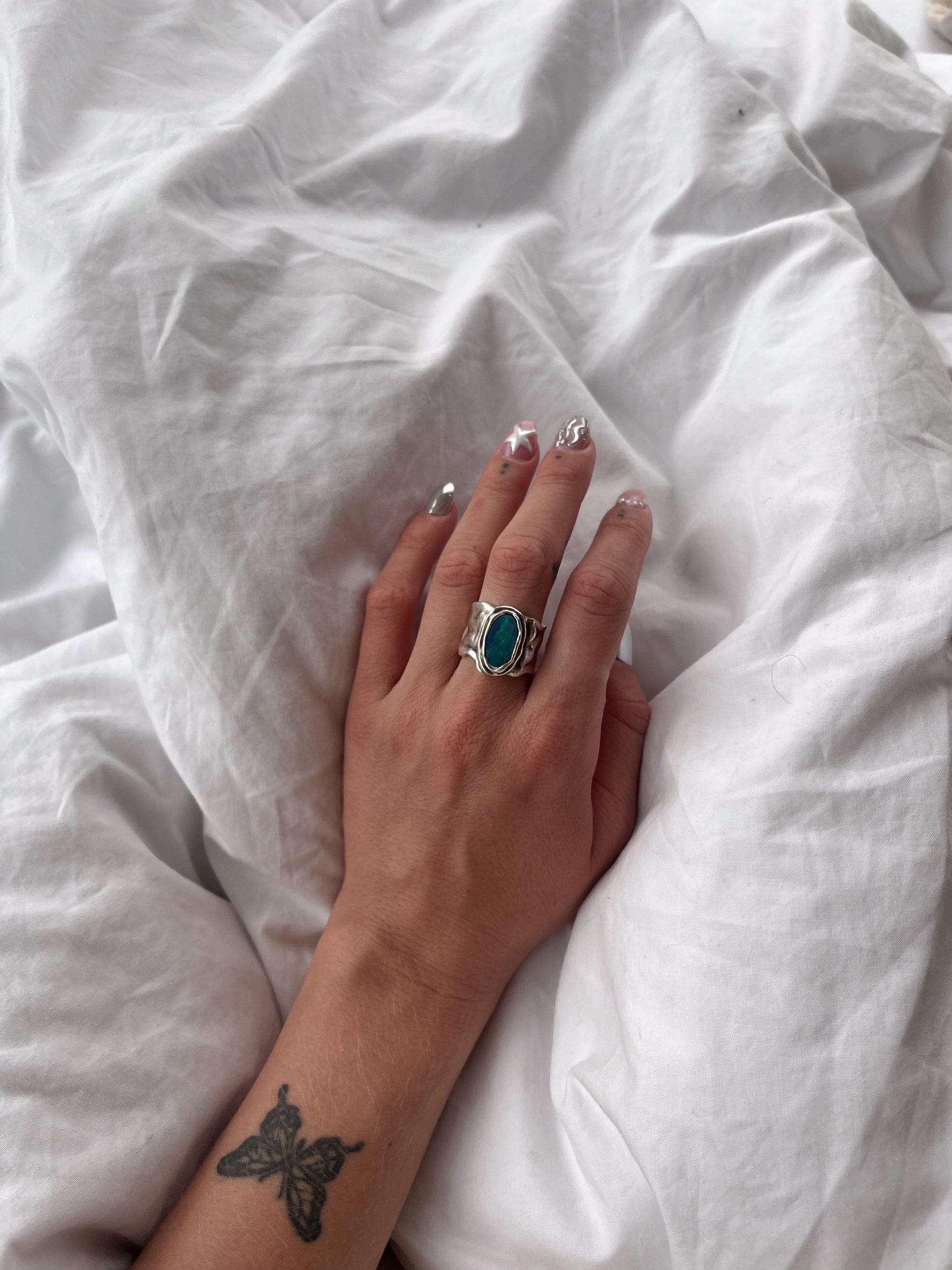 Hand with blue Opal Ring on white sheets