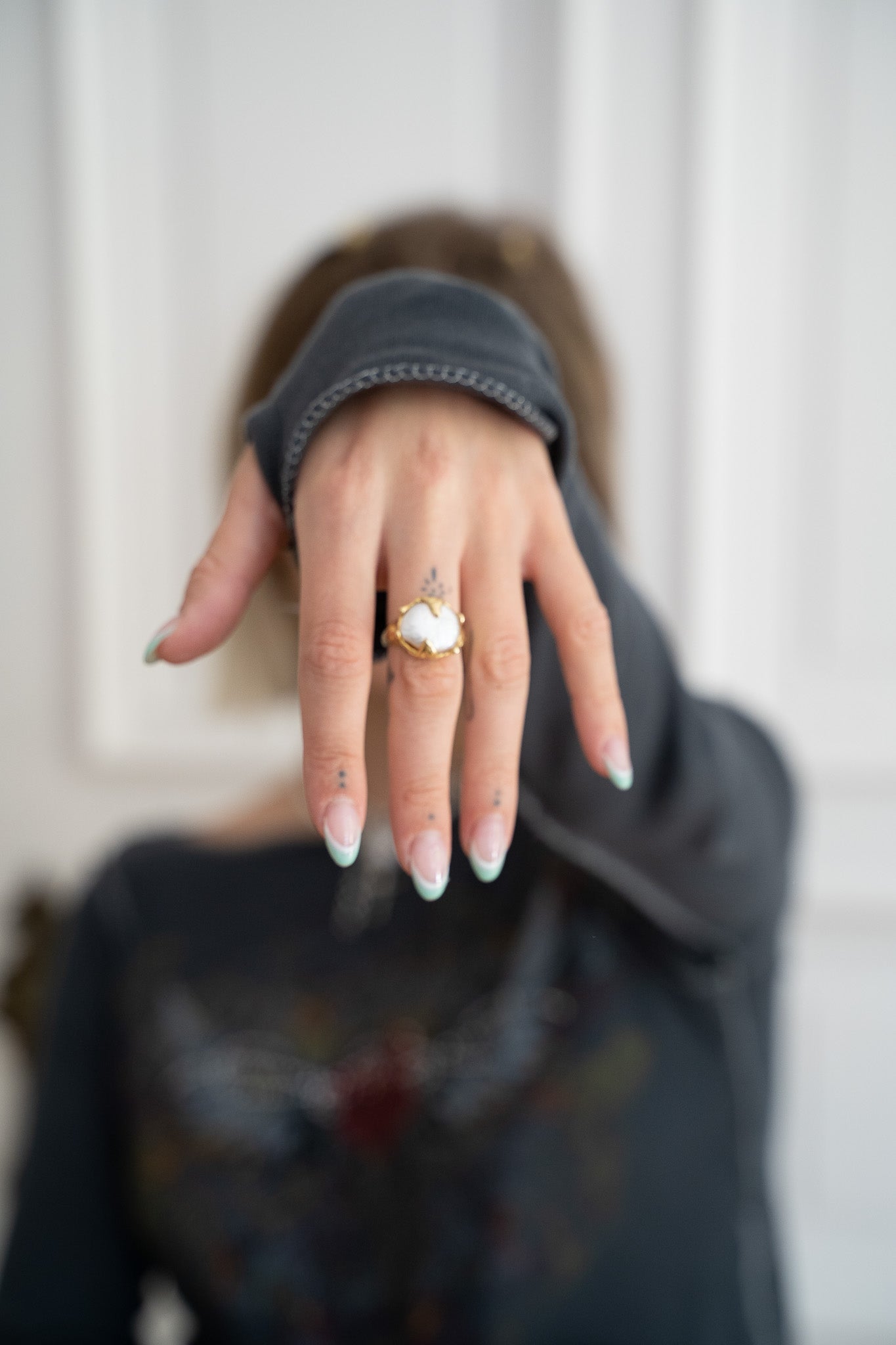 A hand with a gold pearl ring and pretty nails